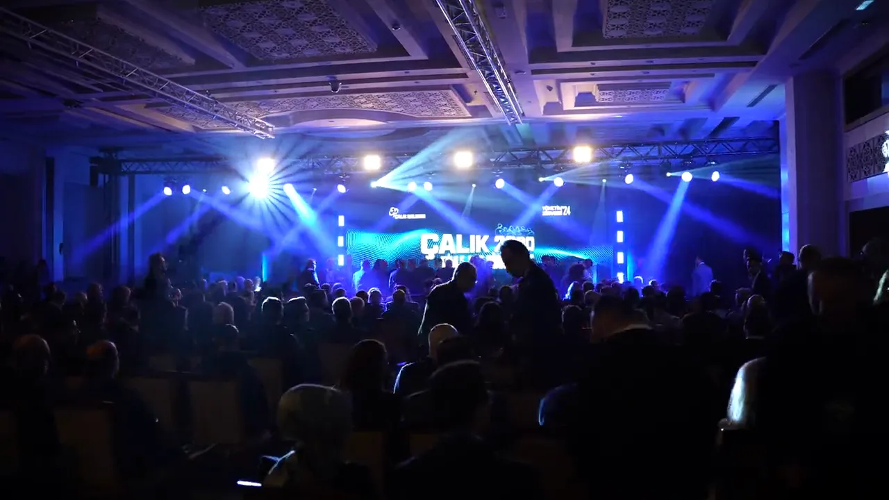 Salon geniş planda: mavi ışıklı sahne ve dolu koltuklar