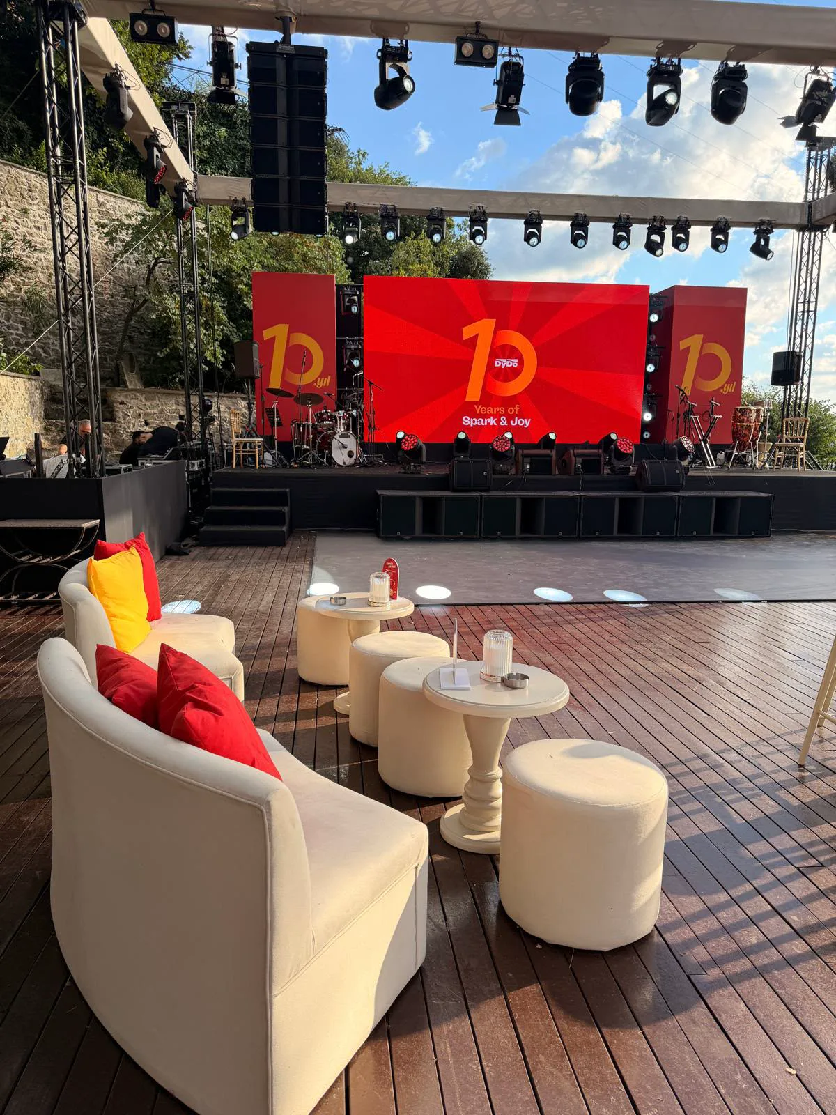 Lounge düzeni: kırmızı ve sarı yastıklı koltuklar, arkada sahne