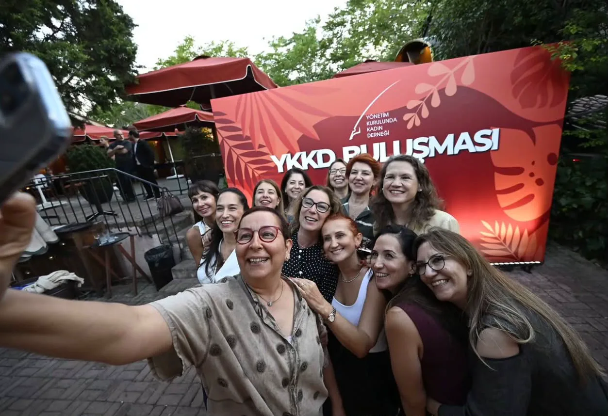 Etkinlik panosunun önünde gülerek özçekim yapan konuklar